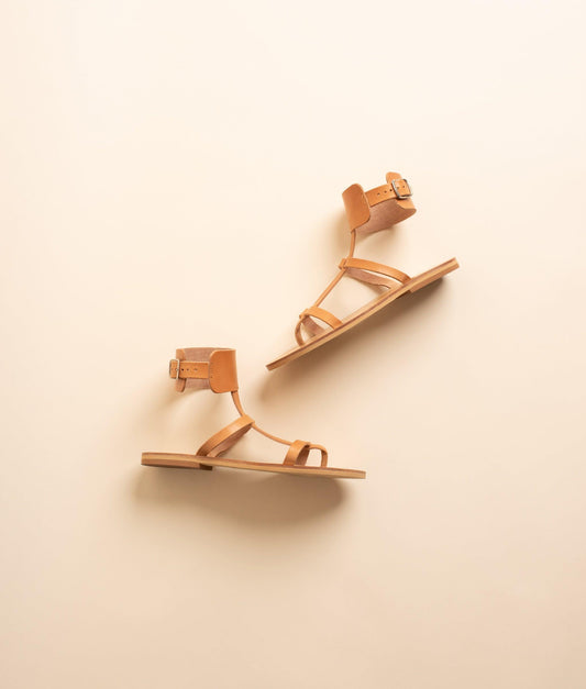 Athena leather flat sandals in tan against a beige background. They are flat sandals buckle.