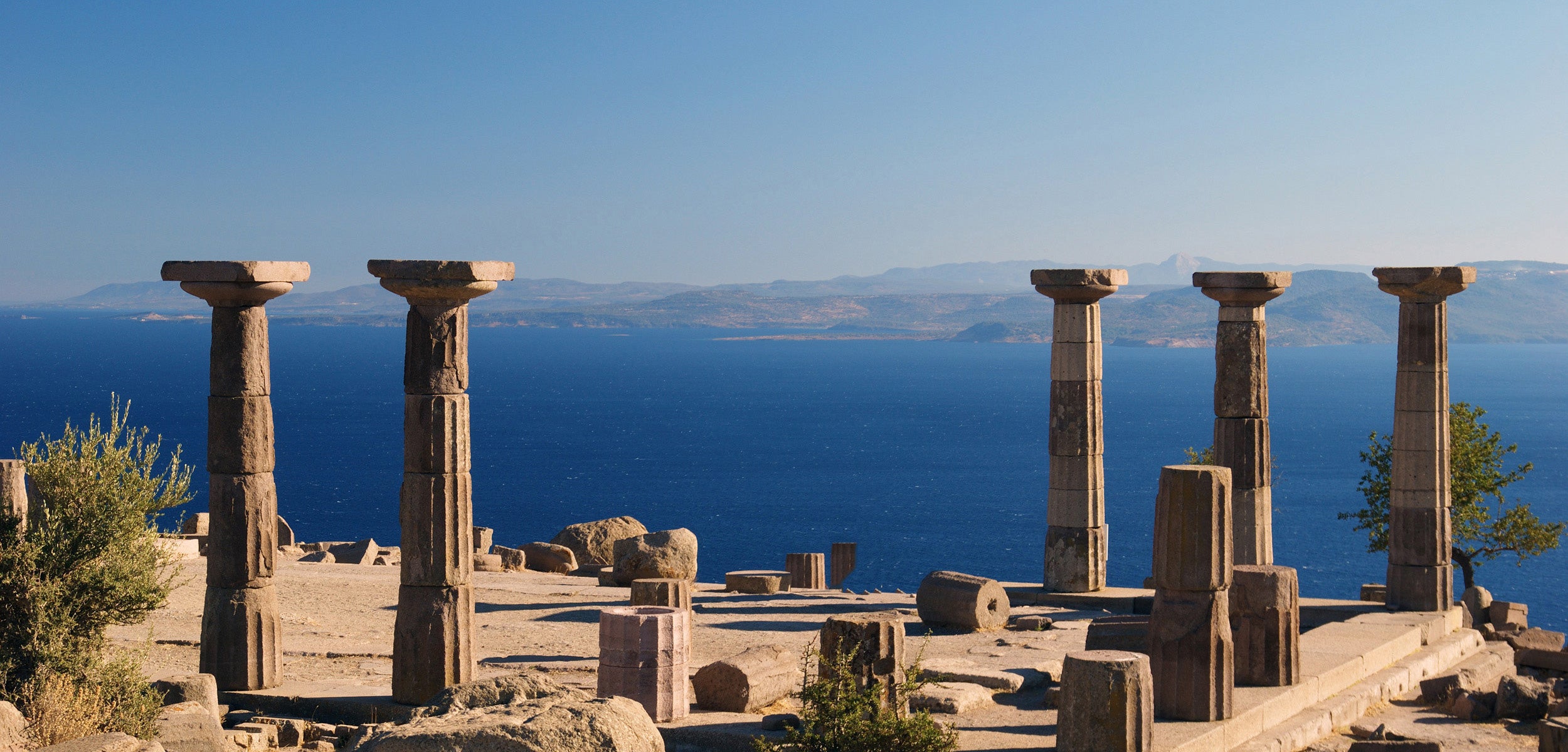 Flat Sandals for Women | An open view of the blue sea behaind ancient columns to symbolize the heritage of our elegant flats which are womens flat leather sandals.