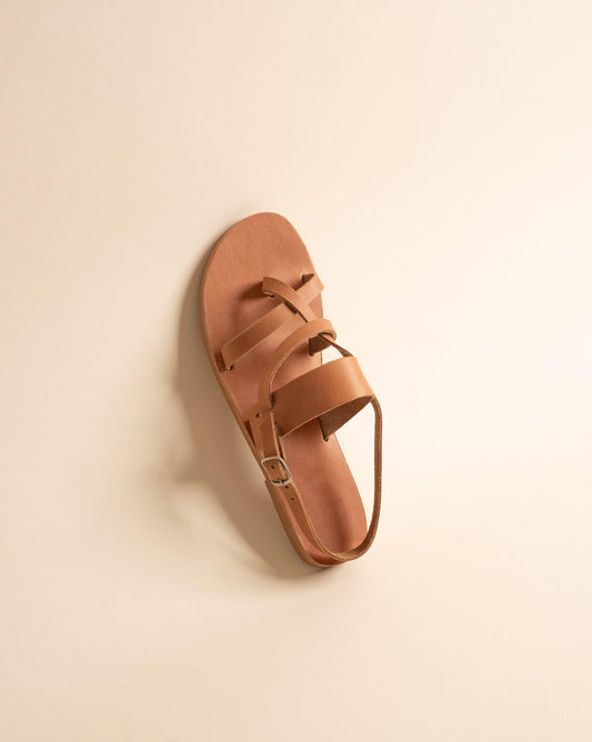 A tan flat sandal against a beige background. They are tan flats womens.