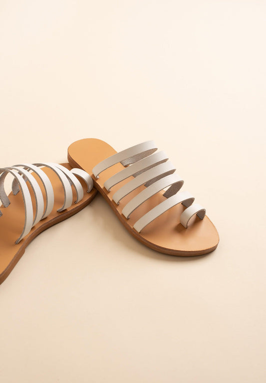Harmonia white sandals against a beige background. These white leather sandals are white flats for women.