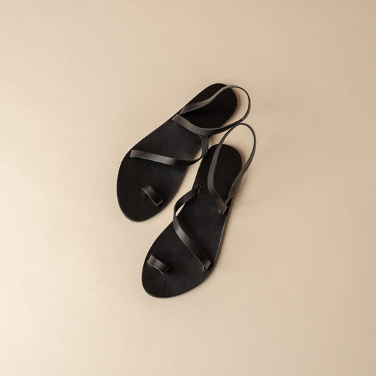 Top view of a pair of fancy black flats on a beige background. These flat sandals black are the perfect flat sandals to wear with dresses.