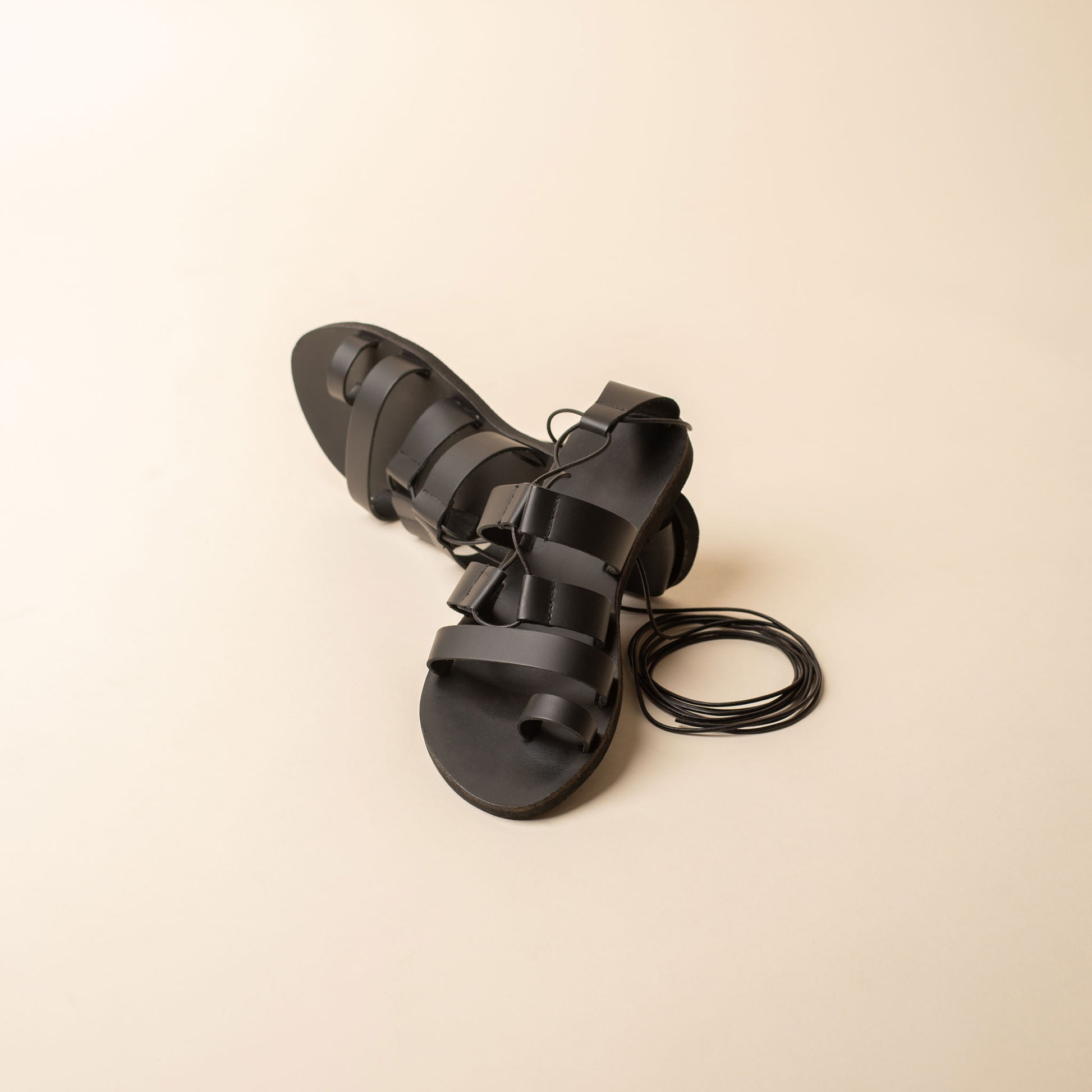 Black leather strappy sandals on a beige background