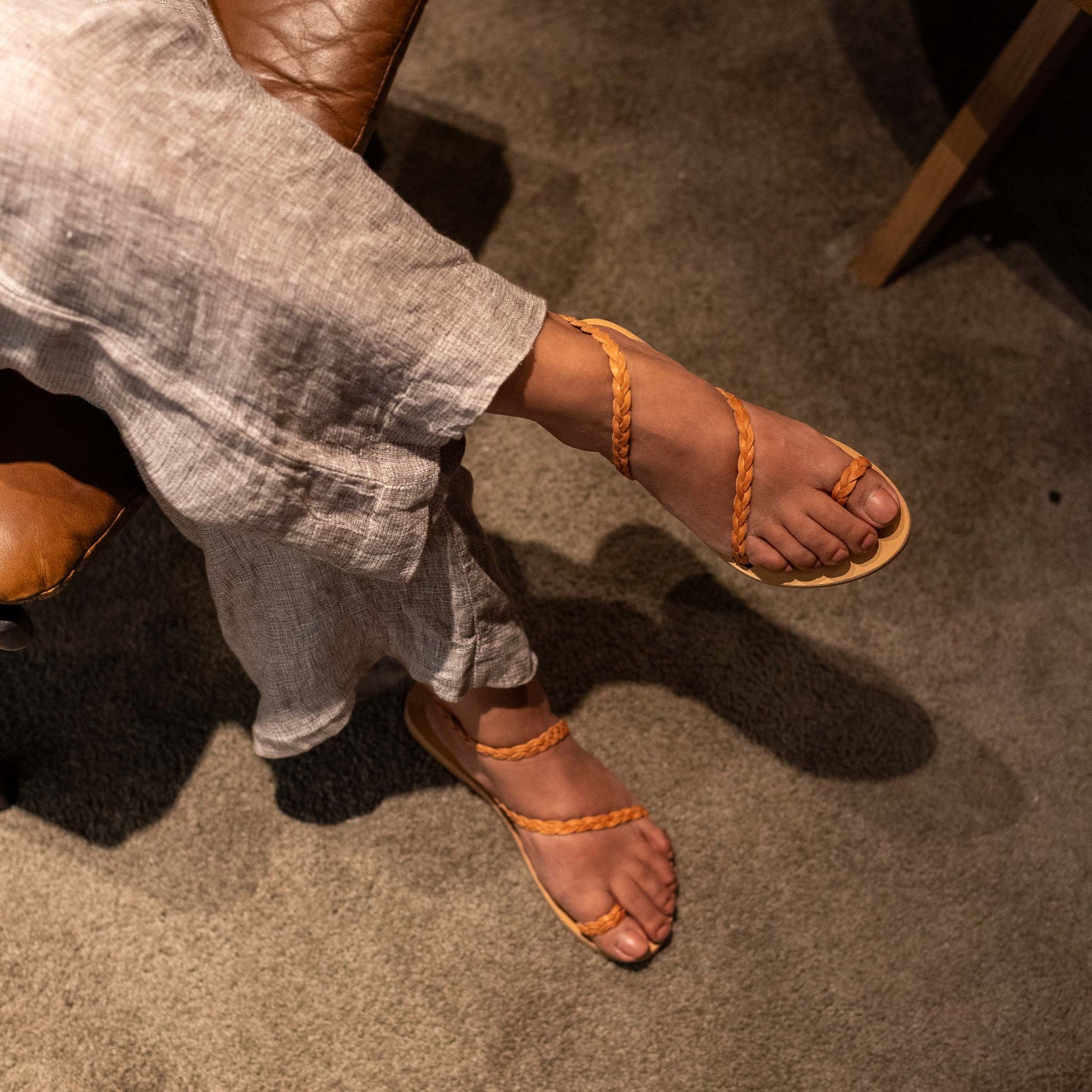 Woman wearing tan sandals for women flat on a carpeted floor