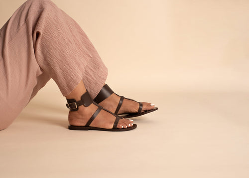 Brown leather sandals for women worn with pink pants on a beige background