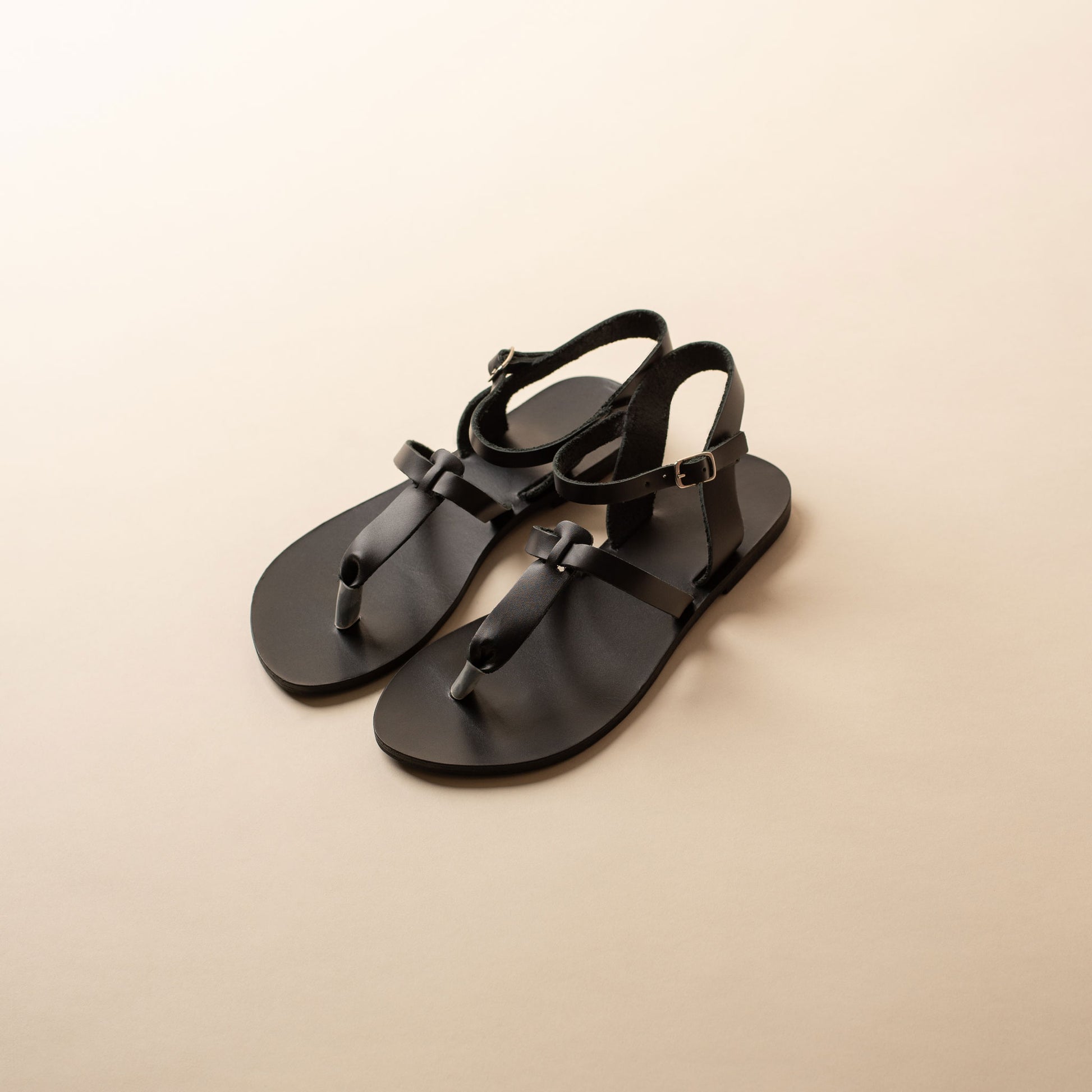 Pair of black flat sandals ankle strap on a beige background